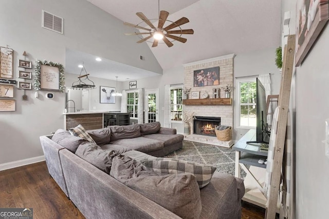 living room with ceiling fan with notable chandelier, a fireplace, high vaulted ceiling, and dark hardwood / wood-style flooring