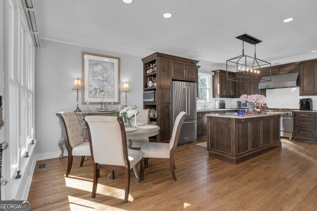 dining space with light hardwood / wood-style floors, a notable chandelier, ornamental molding, and sink