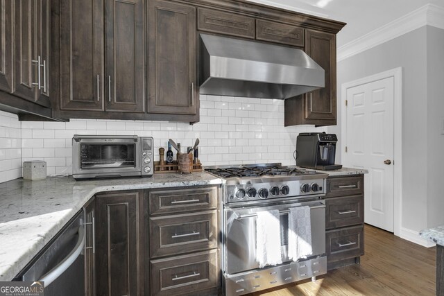 kitchen featuring stainless steel appliances, light stone counters, backsplash, exhaust hood, and crown molding