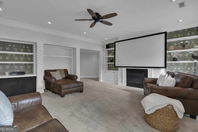 cinema room featuring built in features, ceiling fan, crown molding, and light carpet