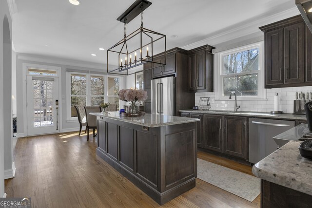 kitchen featuring appliances with stainless steel finishes, light stone countertops, a kitchen island, dark brown cabinets, and decorative light fixtures