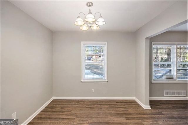 unfurnished room featuring dark hardwood / wood-style flooring, a chandelier, and plenty of natural light