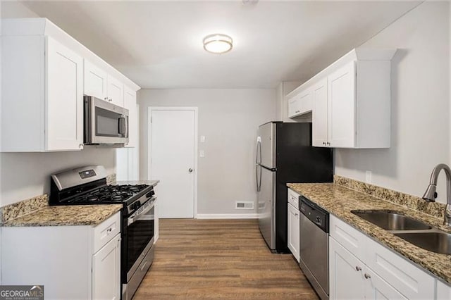 kitchen with light hardwood / wood-style flooring, white cabinetry, dark stone counters, appliances with stainless steel finishes, and sink