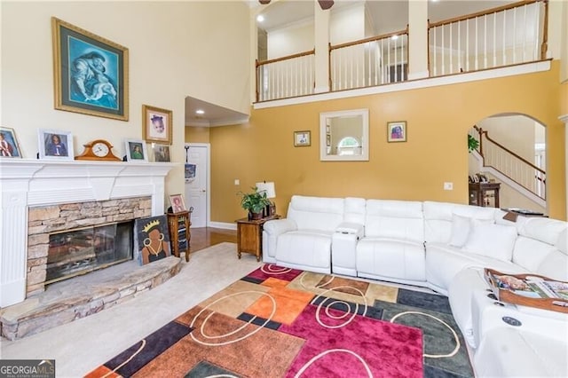 living room with a stone fireplace, a towering ceiling, and carpet