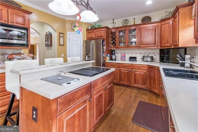 kitchen with appliances with stainless steel finishes, crown molding, a kitchen bar, decorative backsplash, and decorative light fixtures