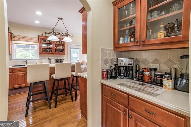 kitchen featuring pendant lighting, light hardwood / wood-style floors, a breakfast bar area, ornamental molding, and sink