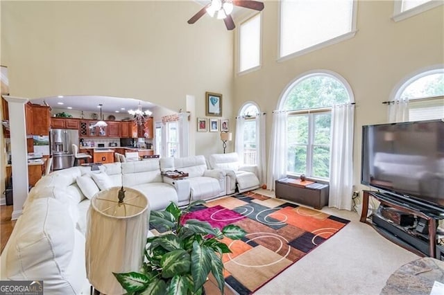 living room with a high ceiling, plenty of natural light, and ceiling fan with notable chandelier