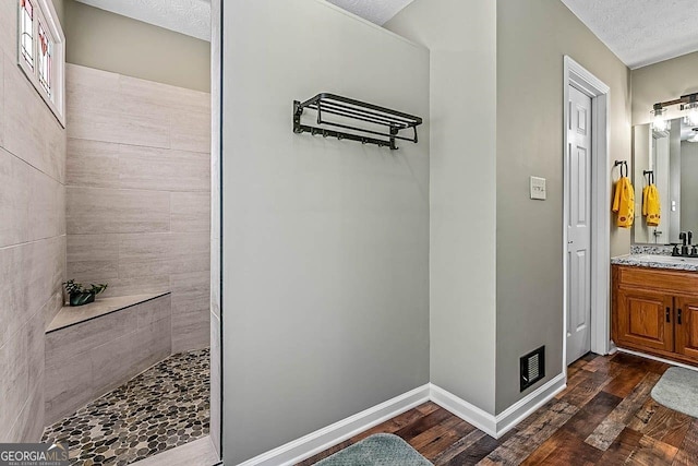 bathroom with a textured ceiling, hardwood / wood-style floors, a tile shower, and vanity