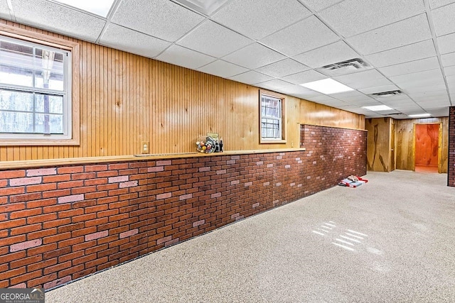 basement with wooden walls, carpet floors, brick wall, and a drop ceiling