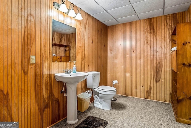 bathroom featuring toilet, wooden walls, and a drop ceiling