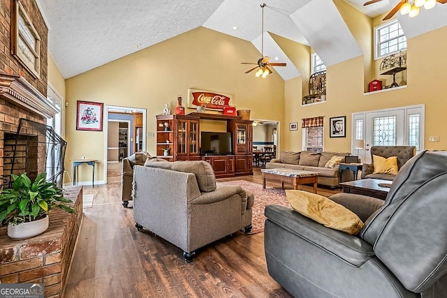 living room with ceiling fan, dark wood-type flooring, high vaulted ceiling, a fireplace, and a textured ceiling