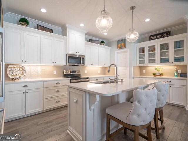 kitchen featuring stainless steel appliances, an island with sink, a breakfast bar, sink, and white cabinetry