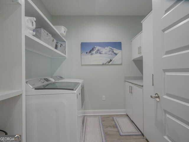 clothes washing area featuring washing machine and dryer, light hardwood / wood-style floors, and cabinets