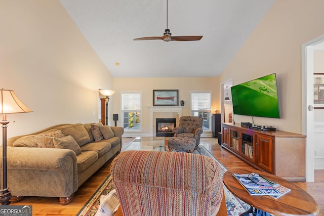 living room with ceiling fan, light hardwood / wood-style floors, high vaulted ceiling, and a fireplace