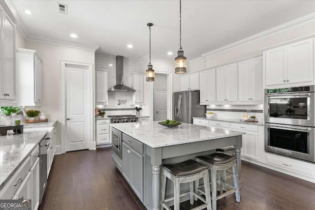 kitchen featuring stainless steel appliances, a breakfast bar, a kitchen island, white cabinets, and wall chimney range hood