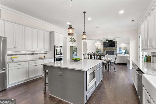 kitchen featuring appliances with stainless steel finishes, decorative light fixtures, white cabinetry, light stone counters, and a stone fireplace