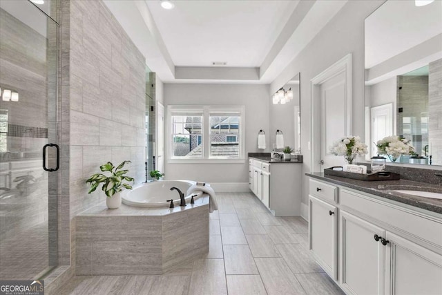 bathroom featuring separate shower and tub, vanity, and a tray ceiling