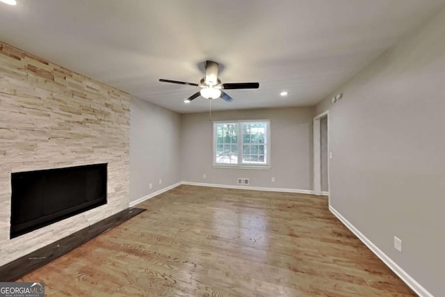 unfurnished living room featuring ceiling fan, wood-type flooring, and a stone fireplace