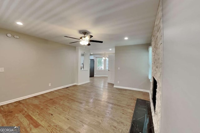 unfurnished living room featuring ceiling fan, a stone fireplace, and hardwood / wood-style flooring