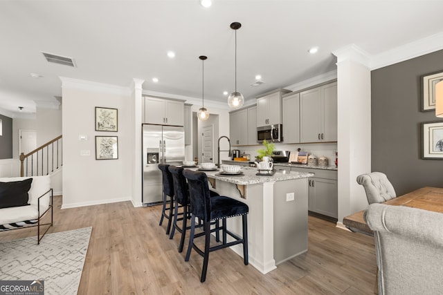 kitchen with a kitchen island with sink, gray cabinetry, stainless steel appliances, crown molding, and pendant lighting