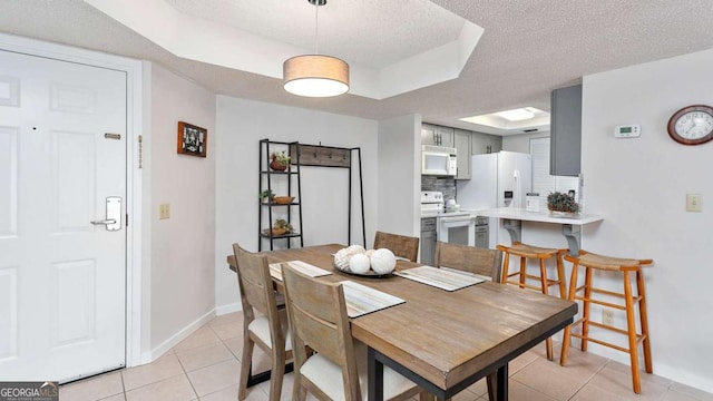 tiled dining room featuring a textured ceiling and a raised ceiling