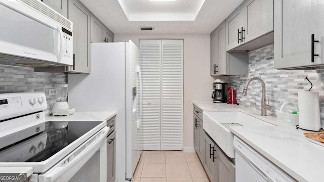 kitchen featuring white appliances, gray cabinets, a tray ceiling, and decorative backsplash