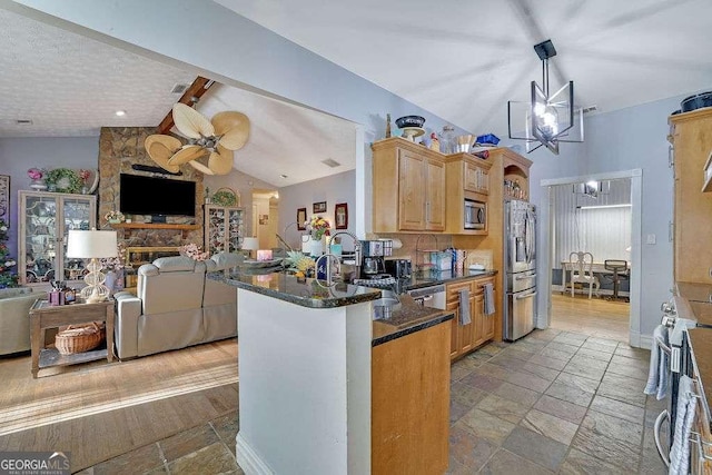 kitchen with sink, lofted ceiling, kitchen peninsula, dark stone counters, and appliances with stainless steel finishes