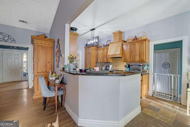 kitchen featuring kitchen peninsula, custom exhaust hood, pendant lighting, decorative backsplash, and an inviting chandelier