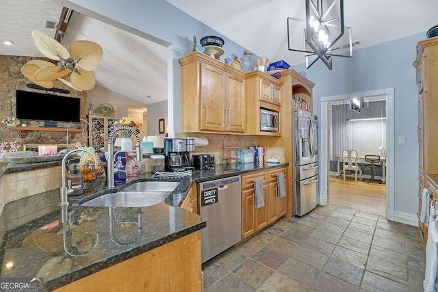 kitchen with decorative light fixtures, stainless steel appliances, ceiling fan with notable chandelier, dark stone countertops, and sink