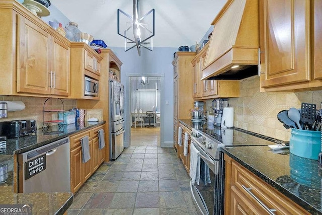 kitchen featuring appliances with stainless steel finishes, premium range hood, a notable chandelier, dark stone counters, and decorative light fixtures