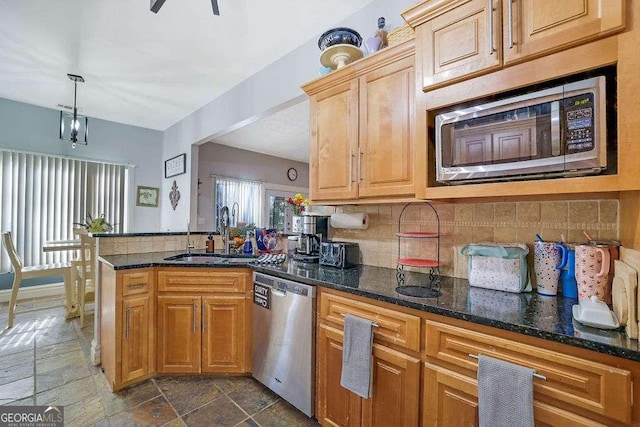 kitchen featuring dark stone countertops, stainless steel appliances, sink, decorative light fixtures, and backsplash