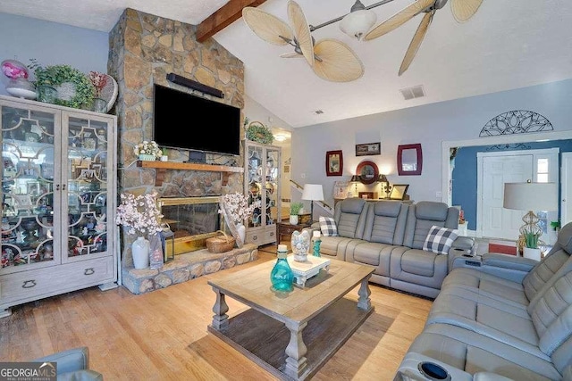 living room with wood-type flooring, ceiling fan, vaulted ceiling with beams, and a stone fireplace