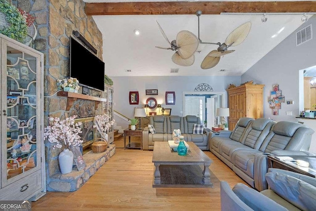 living room with ceiling fan, light wood-type flooring, lofted ceiling with beams, and a fireplace