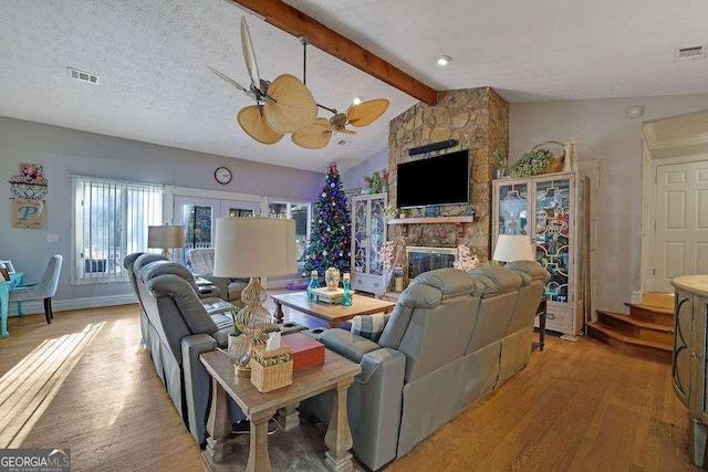 living room featuring a textured ceiling, light hardwood / wood-style flooring, a fireplace, ceiling fan, and vaulted ceiling with beams