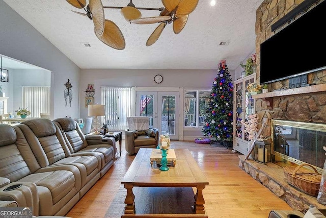 living room with a fireplace, a textured ceiling, french doors, and light hardwood / wood-style floors