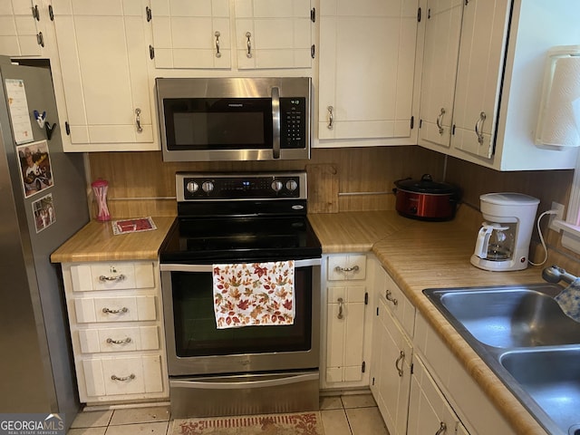 kitchen featuring appliances with stainless steel finishes, white cabinets, sink, and light tile patterned floors