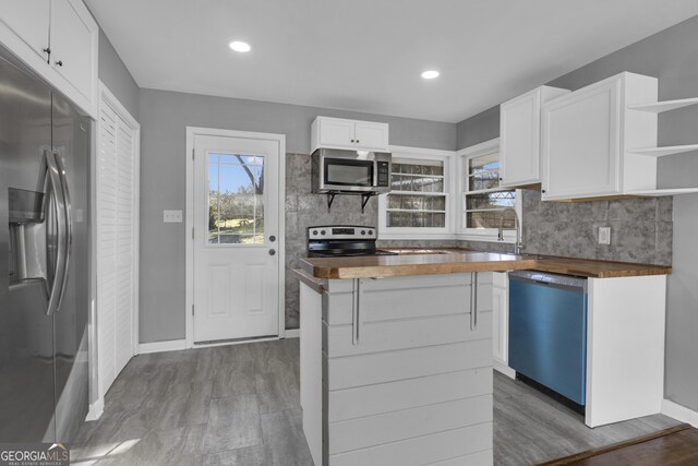 kitchen with appliances with stainless steel finishes, wood counters, white cabinetry, sink, and backsplash