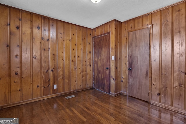 spare room featuring a textured ceiling, dark hardwood / wood-style floors, and wood walls