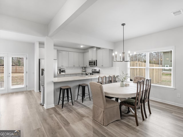 dining space with sink, a wealth of natural light, an inviting chandelier, and light hardwood / wood-style flooring