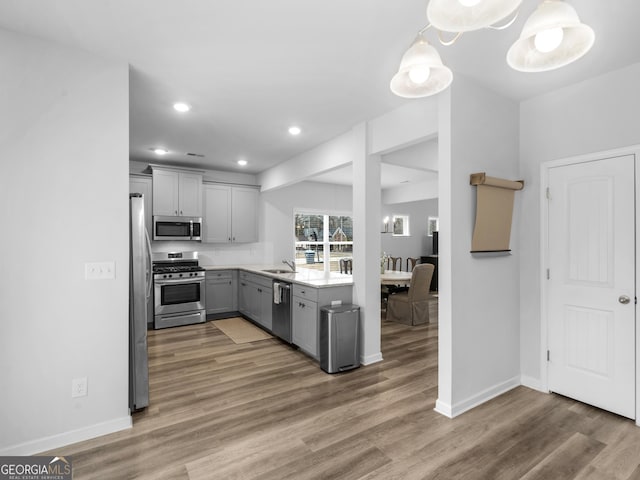 kitchen featuring hardwood / wood-style flooring, stainless steel appliances, decorative light fixtures, and gray cabinetry