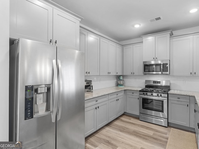 kitchen with stainless steel appliances, gray cabinets, light stone countertops, and light hardwood / wood-style flooring