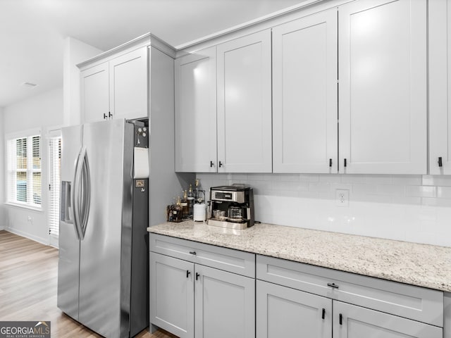 kitchen with light stone counters, stainless steel fridge with ice dispenser, tasteful backsplash, and light hardwood / wood-style floors