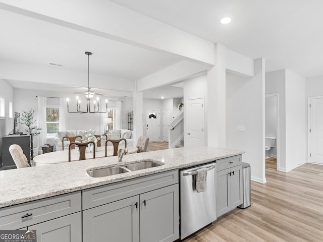 kitchen with sink, gray cabinetry, hanging light fixtures, light stone countertops, and stainless steel dishwasher