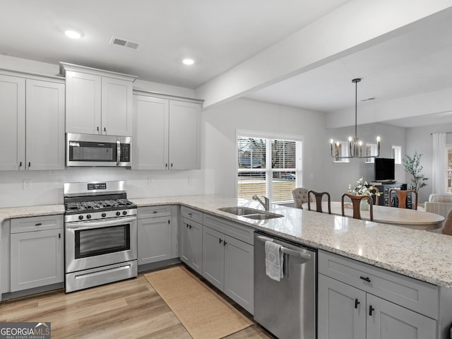 kitchen with sink, gray cabinets, appliances with stainless steel finishes, a notable chandelier, and light hardwood / wood-style floors