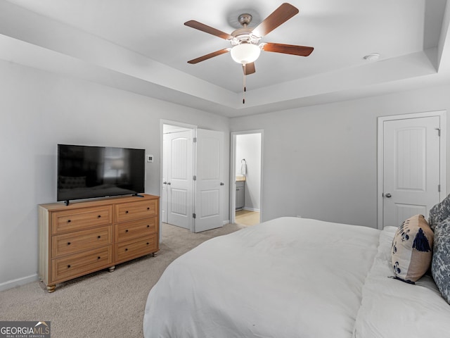 carpeted bedroom with ceiling fan, a raised ceiling, and ensuite bath