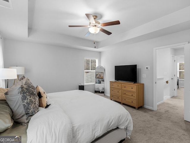 bedroom featuring a tray ceiling, light colored carpet, and ceiling fan