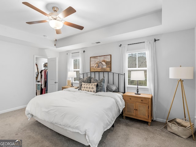 carpeted bedroom featuring a tray ceiling, a spacious closet, ceiling fan, and a closet