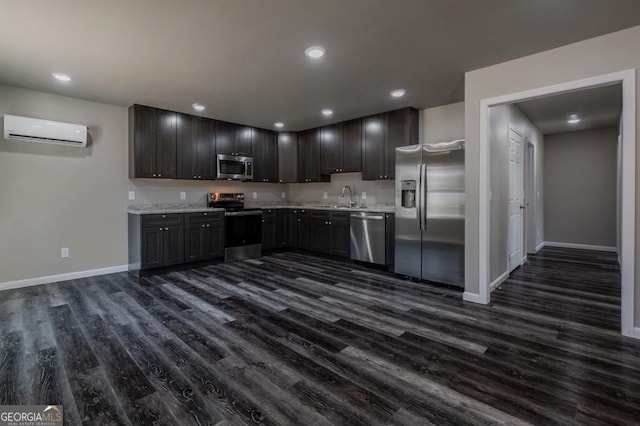 kitchen with a sink, baseboards, appliances with stainless steel finishes, a wall mounted AC, and dark wood-style flooring