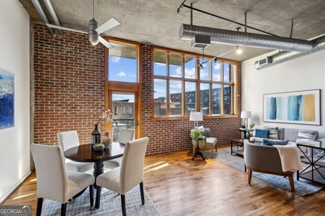 dining room with hardwood / wood-style floors, ceiling fan, a high ceiling, and brick wall