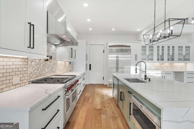 kitchen featuring light wood-type flooring, a sink, white cabinetry, wall chimney exhaust hood, and built in appliances